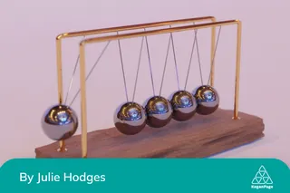 Newton’s cradle on a pink background with one ball moving.