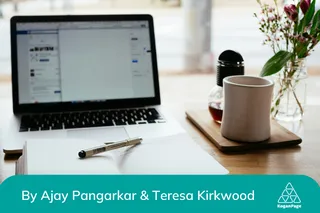 Laptop on desk next to open notebook with a pen and a mug.