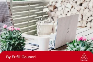 A laptop, mug and flowers on a wooden table.