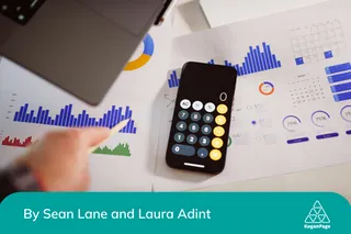 A phone calculator sitting on top of a table with numerous spreadsheets full of metrics with a laptop beside it