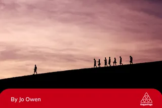 A group of sillhouetted people following  a leader down a path. 