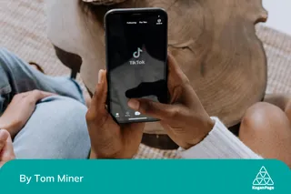 Person on their phone, sitting next to a colleague, and have just opened the TikTok app.