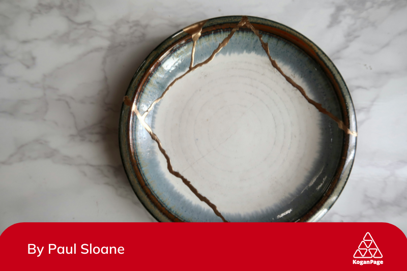 Broken ceramic blue and white plate repaired using kintsugi, with gold-filled cracks on a marbled white surface. 
