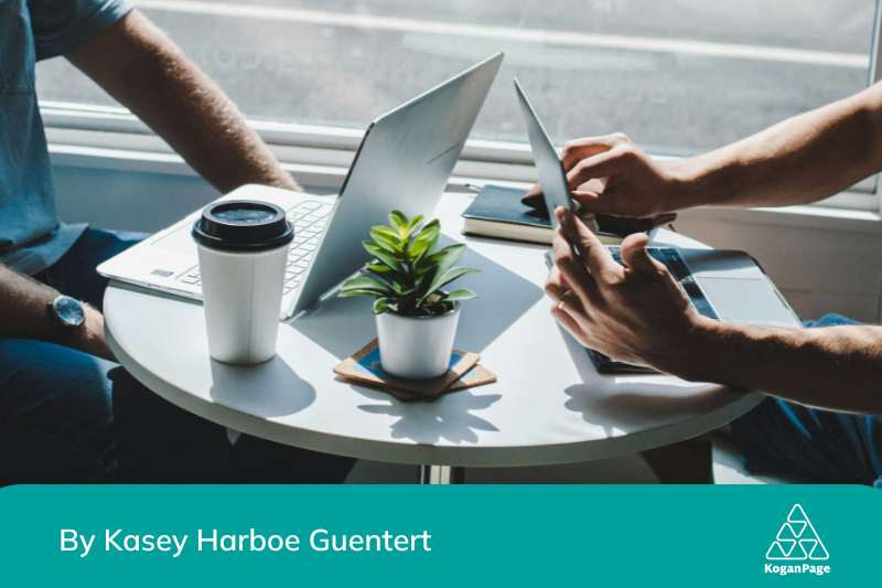 Round coffee table with a plant, two laptops and people sitting either side - can't see their faces, but their hands are in shot.